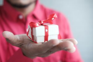 a man holding a white gift box with a red ribbon Best Retirement Gifts for Men