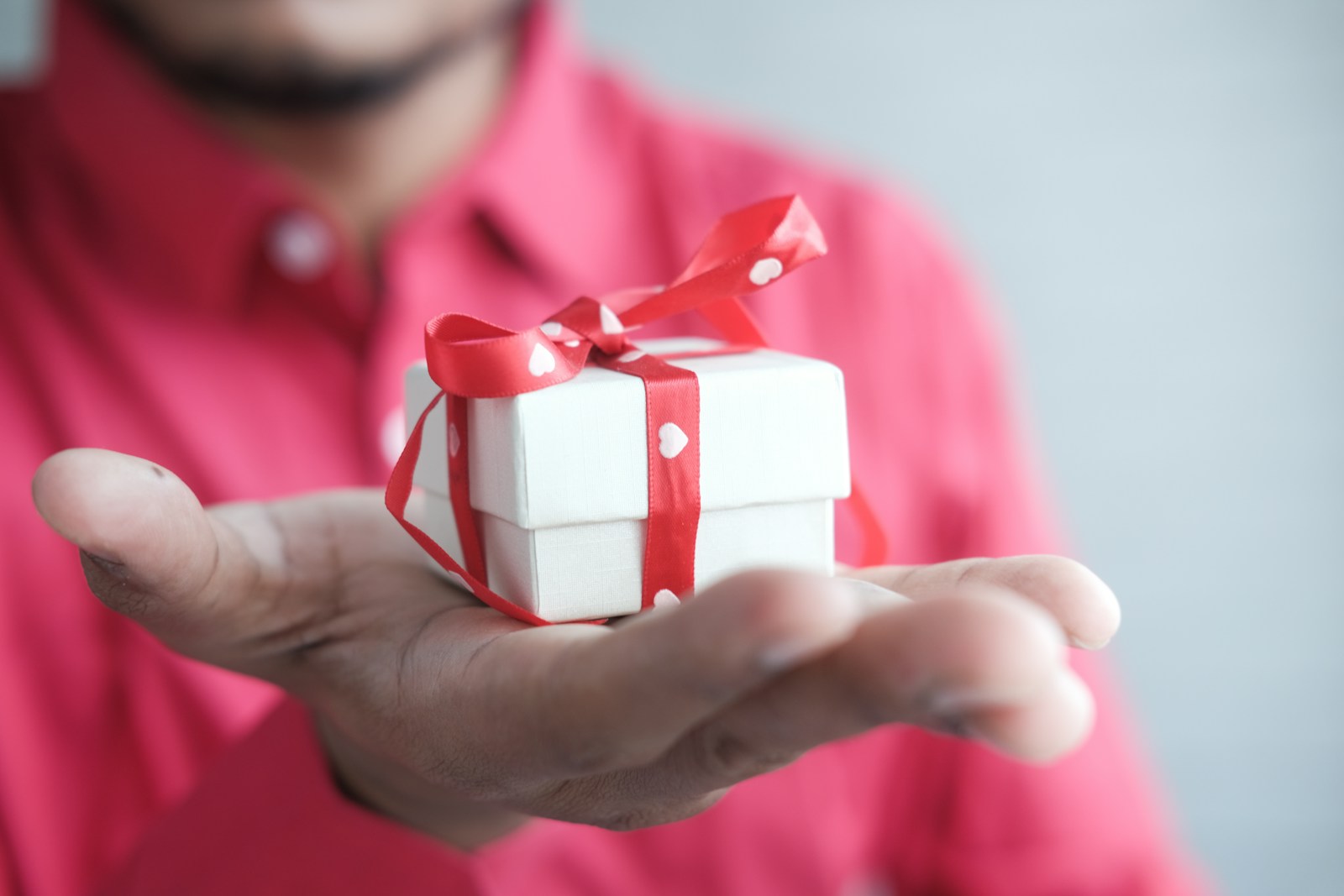 a man holding a white gift box with a red ribbon Best Retirement Gifts for Men